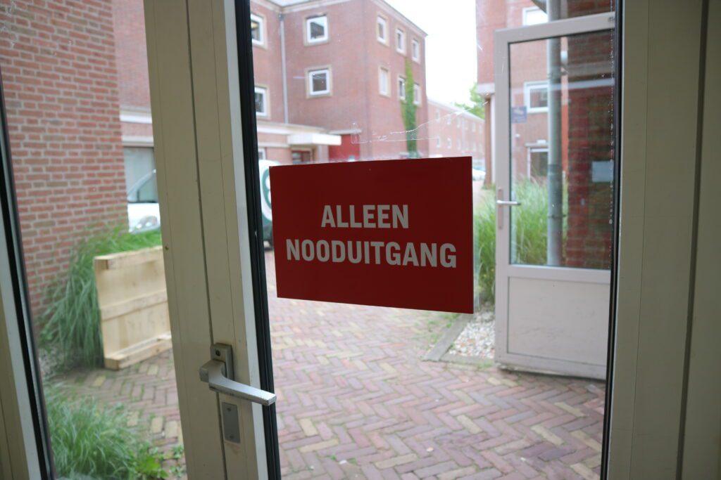 Glazen nooduitgang met het rode bord ‘Alleen nooduitgang’.