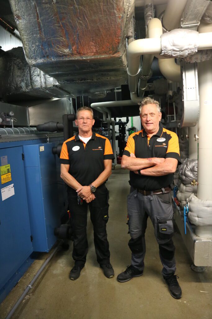 Ruud en Willem van de Technische Dienst staan tussen de technische installaties van woonzorglocatie Insula Dei.